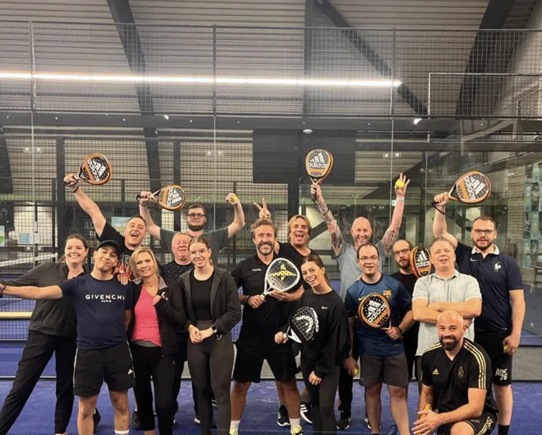 Groepsfoto van 4everyware medewerkers in sportkleding met padelrackets op een padelbaan